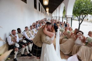 Novios dándose el primer beso tras la ceremonia en su boda en Bodegas Fundador rodeados de invitados emocionados fotografía de EsebeWedding